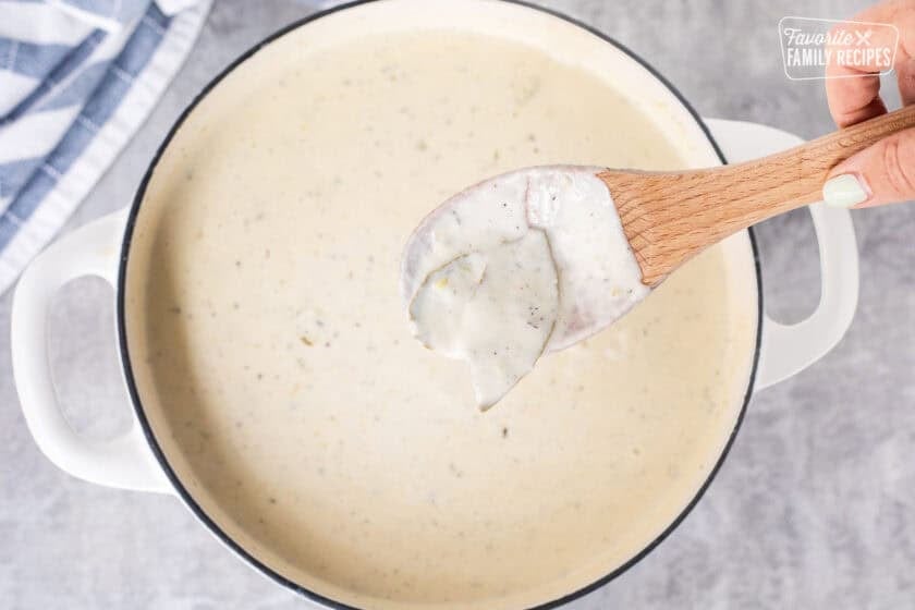 Wooden spoon lifting bay leaves out of soup mixture.