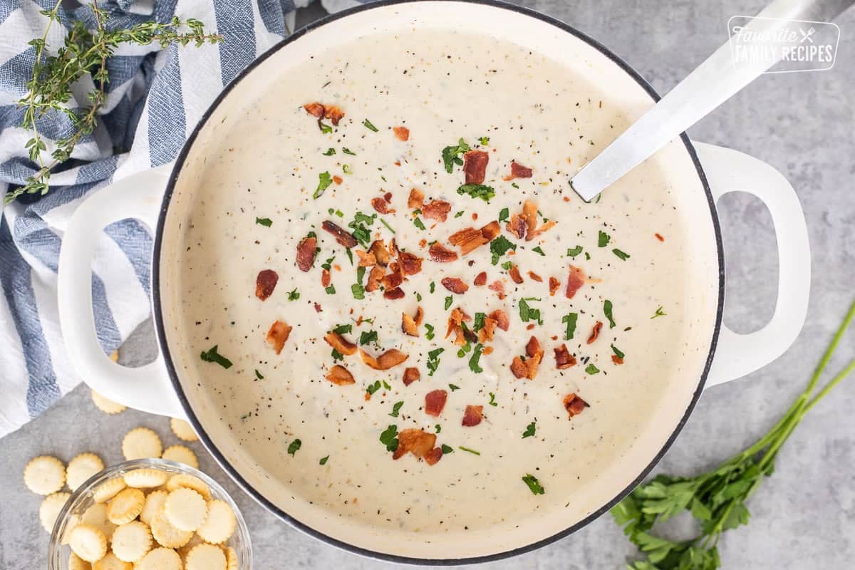Ladle resting in a pot full of clam chowder with fresh clams and garnished with bacon, pepper and fresh parsley.