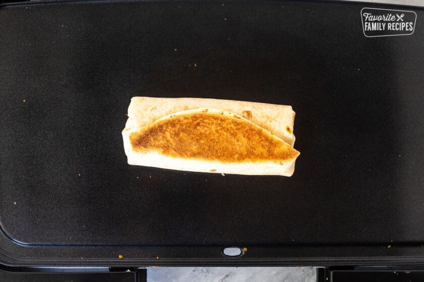 Rolled up quesarito flipped on a skillet.