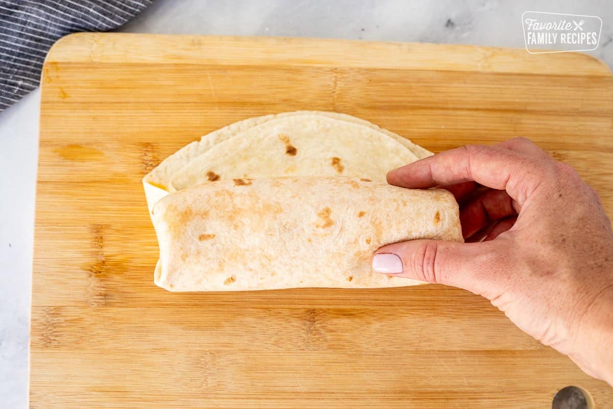 Rolling quesarito into a burrito shape on a cutting board.