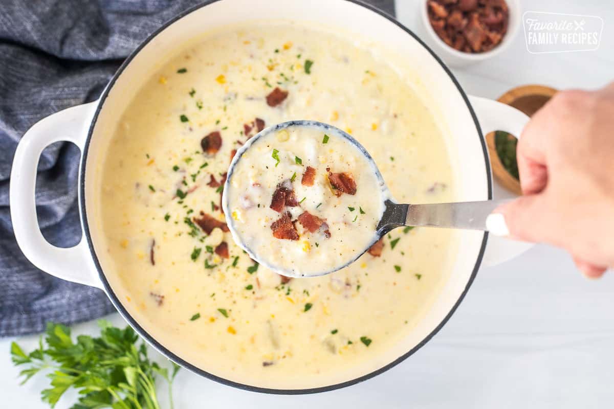 Ladle filled with corn chowder and bacon being lifted from a full pot of chowder