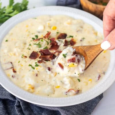 Wooden spoon dipped in Corn Chowder in a bowl with bacon garnish