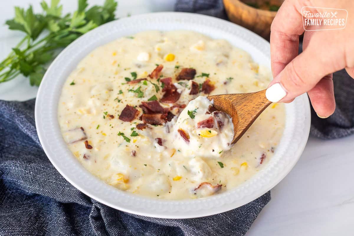 Wooden spoon dipped in Corn Chowder in a bowl with bacon garnish