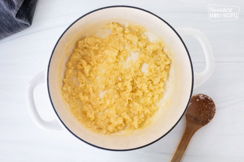 Large pot cooking onions and flour mixed with a wooden spoon for corn chowder with bacon.