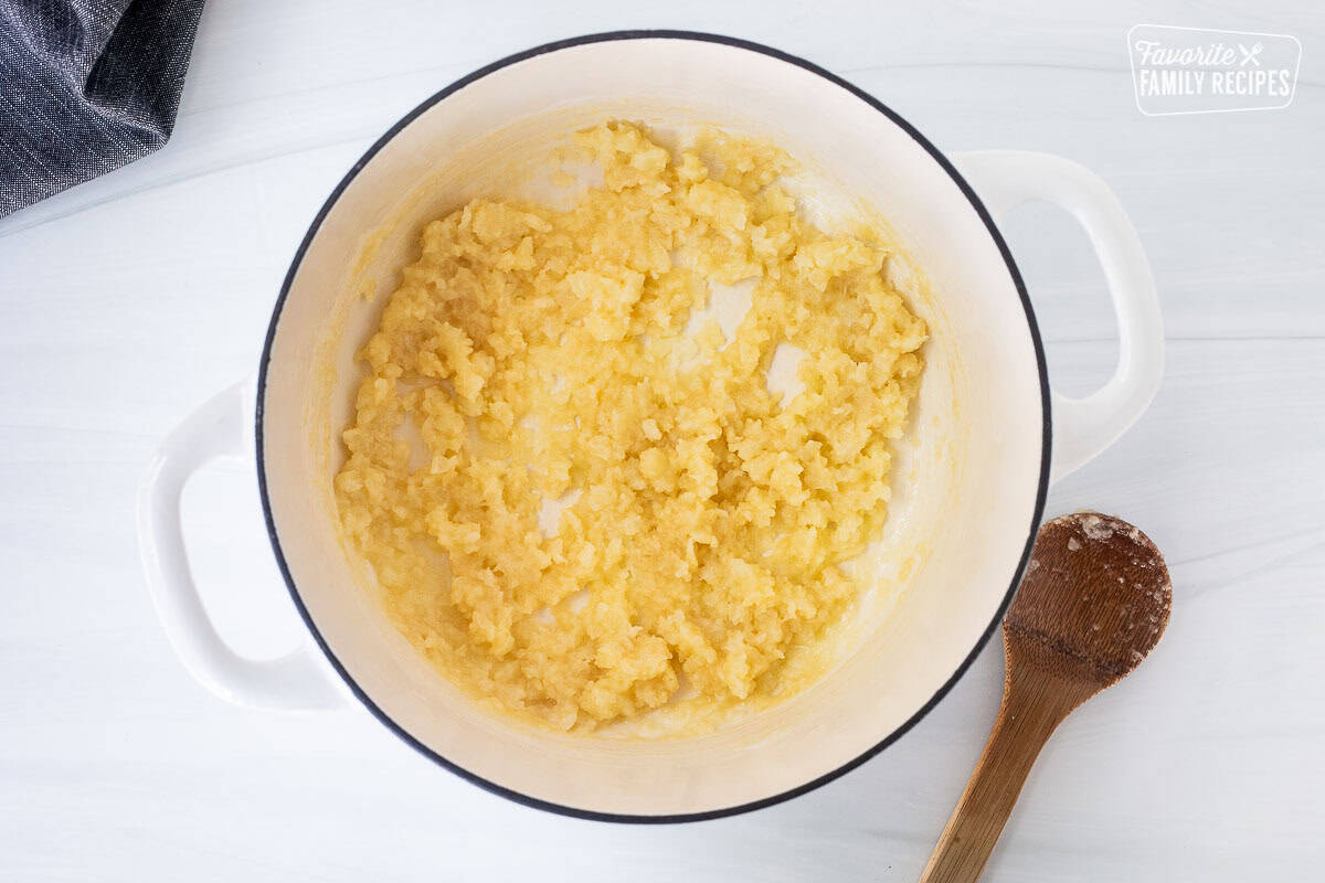 Large pot cooking onions and flour mixed with a wooden spoon for corn chowder with bacon.