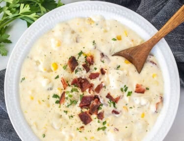 A large bowl of corn chowder with bacon with a spoon resting on the side