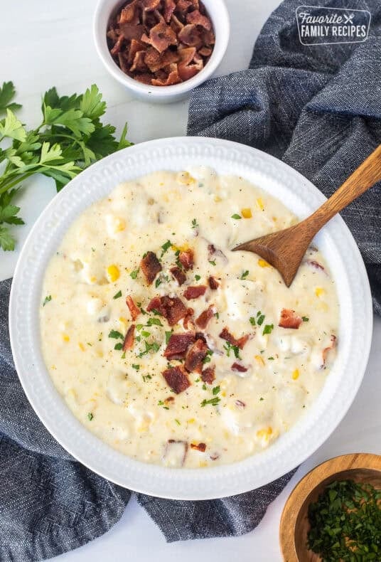 A large bowl of corn chowder with bacon with a spoon resting on the side