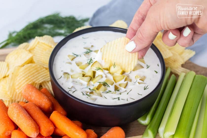 Hand dipping a ruffle chip into the bowl of dill pickle dip.