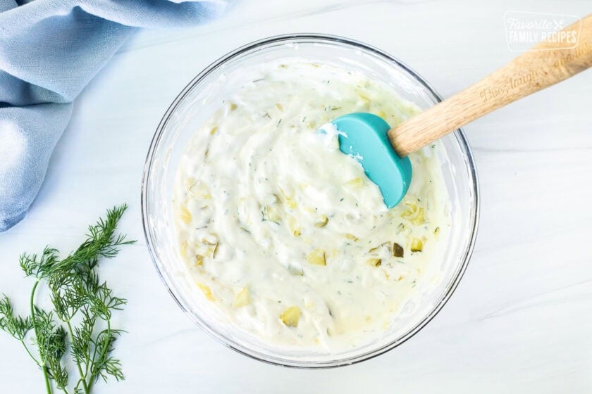Mixing dill pickle dip in a glass mixing bowl with a spatula.