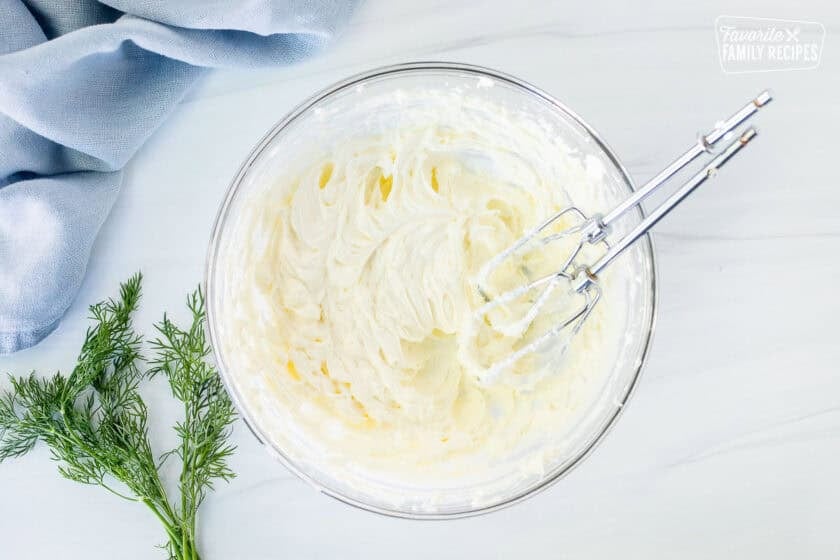 Glass mixing bowl with whipped cream cheese and electric beaters.