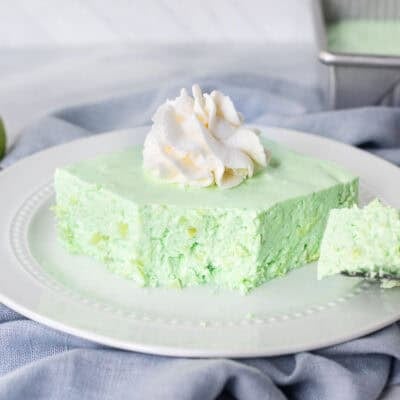 Corner cut on slice of Lime Jello Salad on a plate with whipped cream on top.