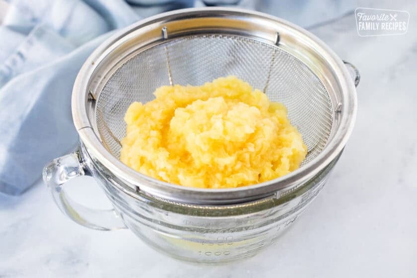 Crushed pineapple draining through a colander into a bowl.