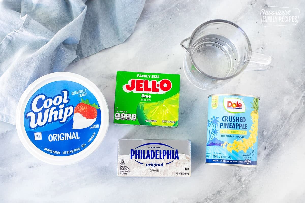 Ingredients to make lime jello salad including lime jello, crushed pineapple, cream cheese, Cool Whip and boiling water.