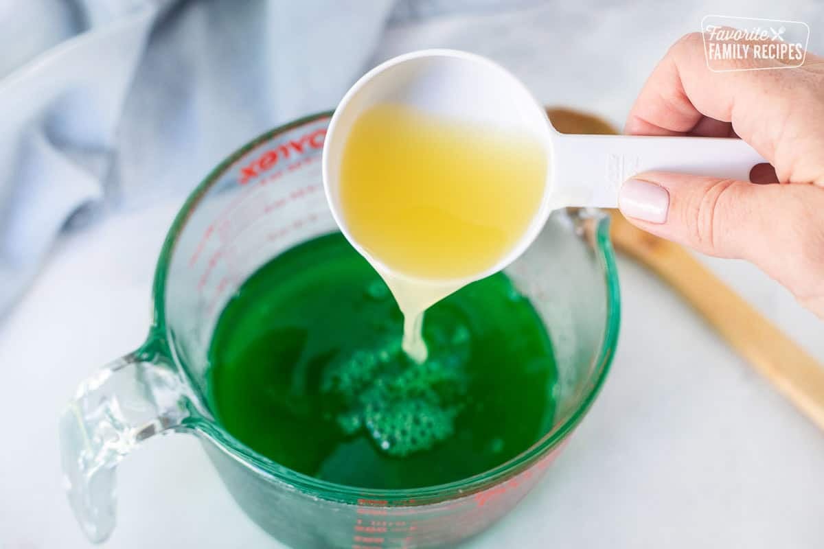 Pouring pineapple juice into a bowl of lime jello.