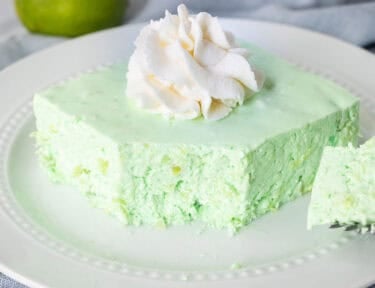Corner cut on slice of Lime Jello Salad on a plate with whipped cream on top.