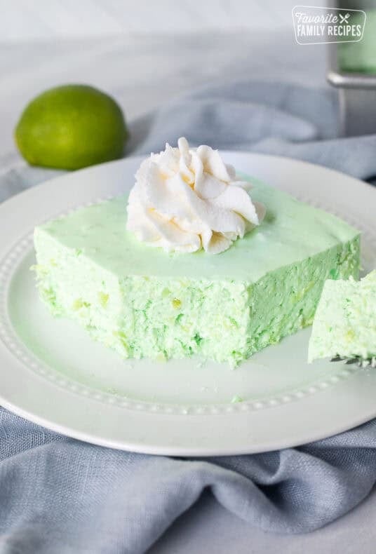Corner cut on slice of Lime Jello Salad on a plate with whipped cream on top.