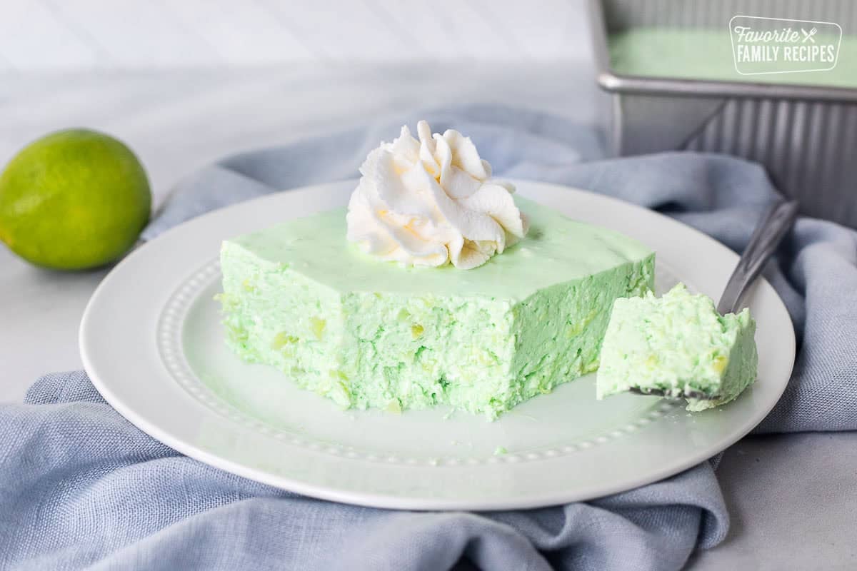 Corner cut on slice of Lime Jello Salad on a plate with whipped cream on top.