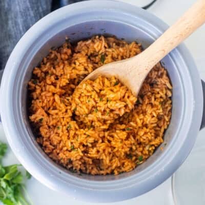 Wooden spoon resting in a rice cooker with Mexican rice.