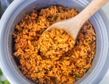Wooden spoon resting in a rice cooker with Mexican rice.
