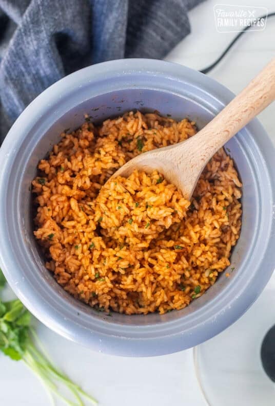 Wooden spoon resting in a rice cooker with Mexican rice.