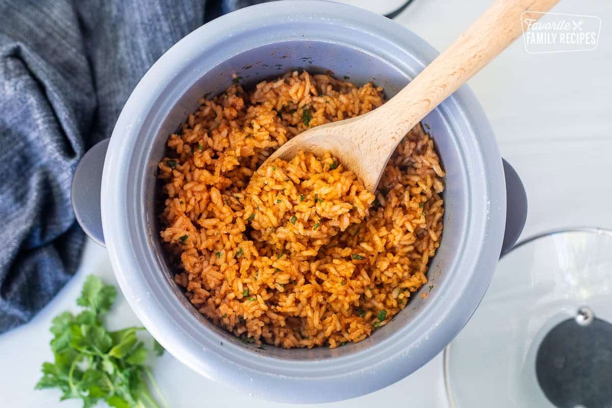 Wooden spoon resting in a rice cooker with Mexican rice.