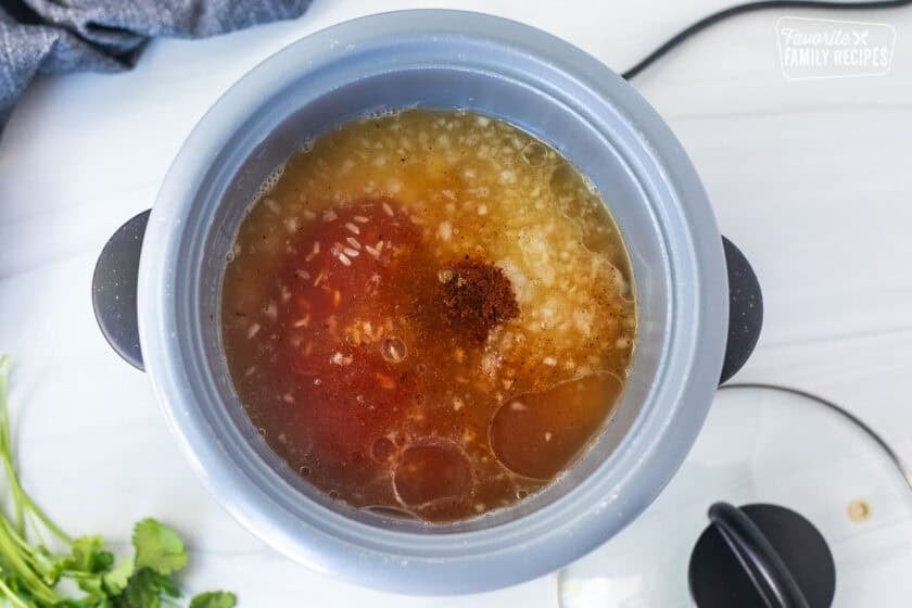 Rice cooker with rice, chicken broth, onion, spices and oil.