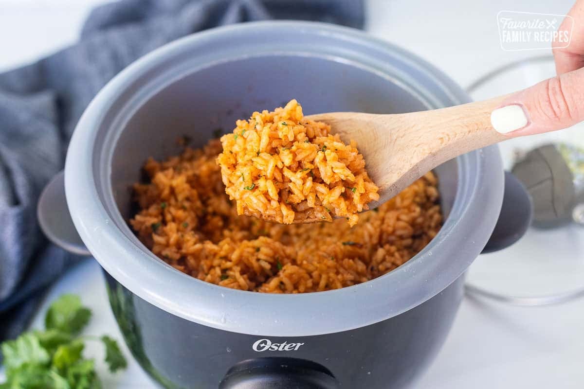 Wooden spoon with Mexican rice lifted from a rice cooker.