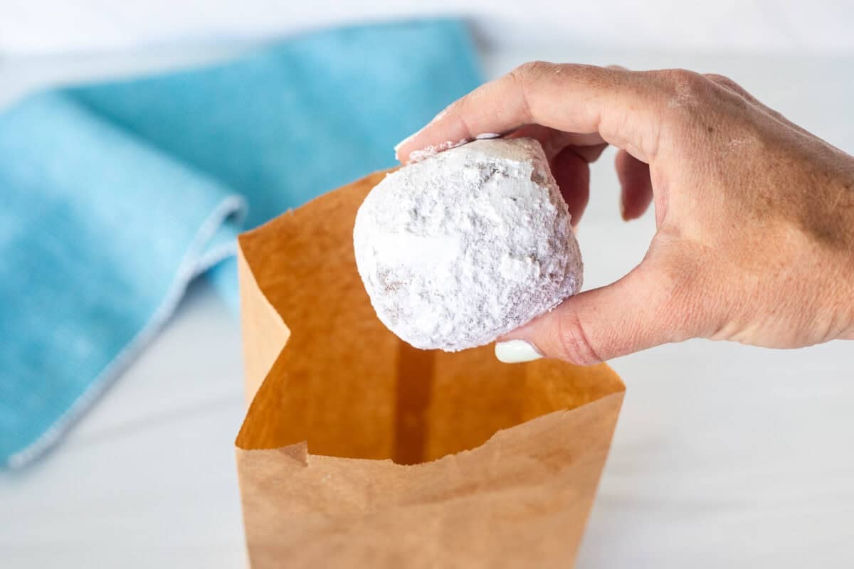 Hand grabbing a New Orleans style beignet out of a paper bag with powdered sugar.