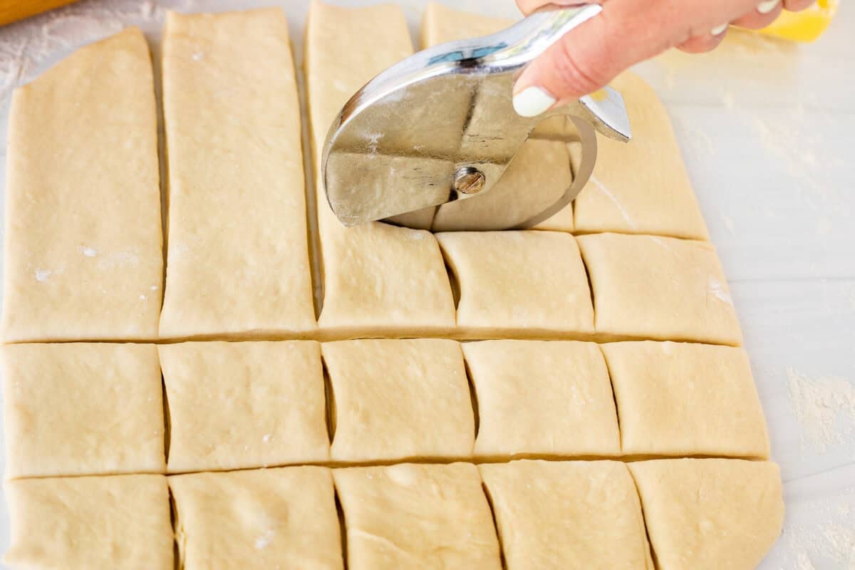 Cutting square pieces of beignet dough with a pizza cutter.