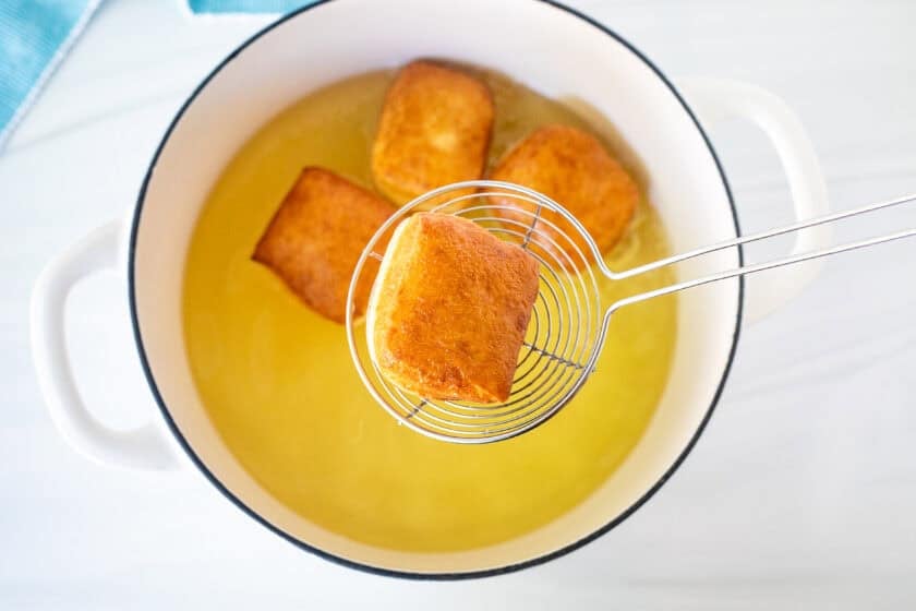 Lifting a golden New Orleans style beignet from a pot of hot oil.