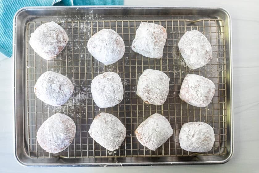 New Orleans style beignets covered in powdered sugar on a wire rack.