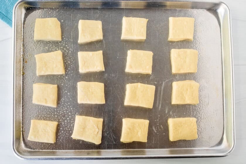 Square cut pieces of New Orleans style beignets dough on a sheet pan.