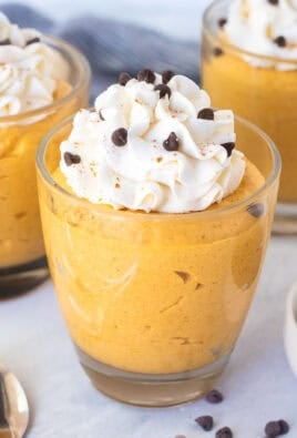 Three glasses of pumpkin mousse topped with whipped cream and mini chocolate chips.