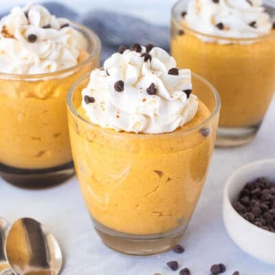 Three glasses of pumpkin mousse topped with whipped cream and mini chocolate chips.