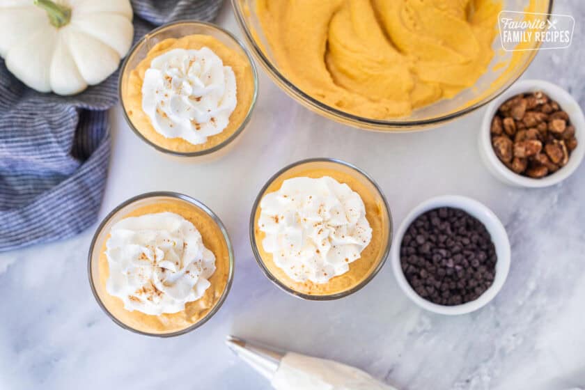Whipped cream pipped onto glasses of pumpkin mousse topped with cinnamon.