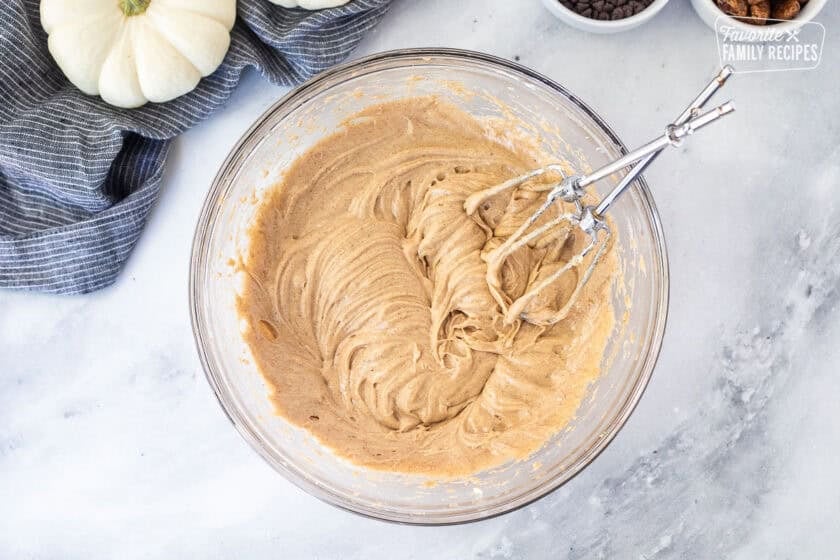 Glass mixing bowl of whipped cream cheese and pumpkin pie spice with electric beaters.
