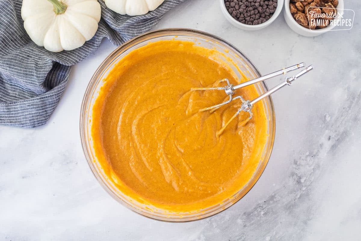 Glass mixing bowl of chipped cream cheese, pumpkin pie spice and pure pumpkin with electric beaters.