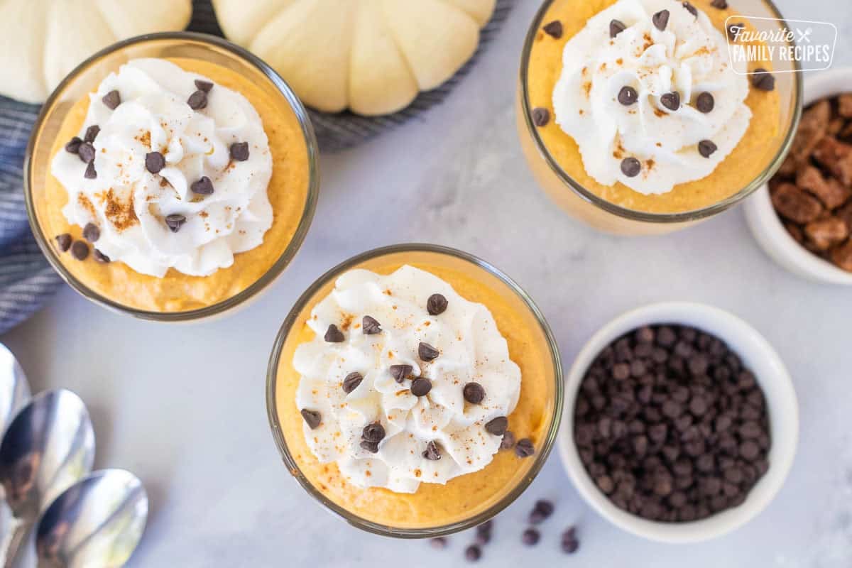 Pumpkin mousse in glasses topped with whipped cream, cinnamon and mini chocolate chips.