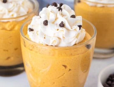 Three glasses of pumpkin mousse topped with whipped cream and mini chocolate chips.