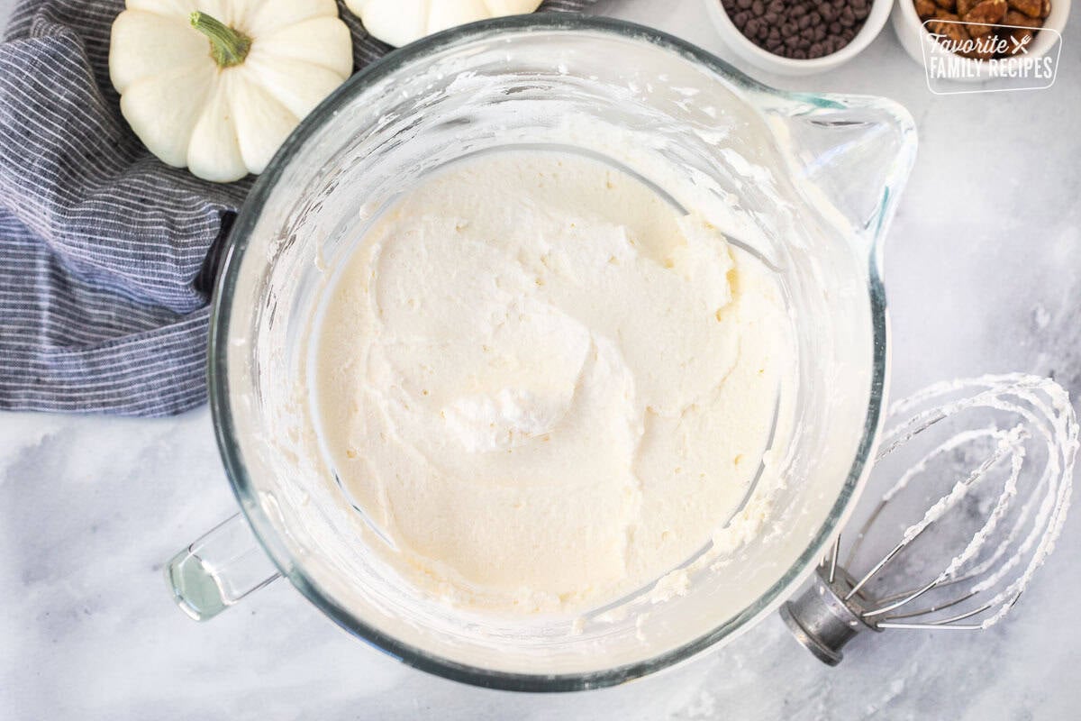 Glass mixing bowl with whipped cream and whisk attachment on the side.