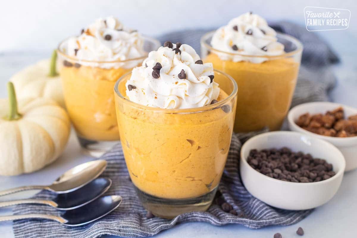 Glasses of pumpkin mousse topped with whipped cream and mini chocolate chips.
