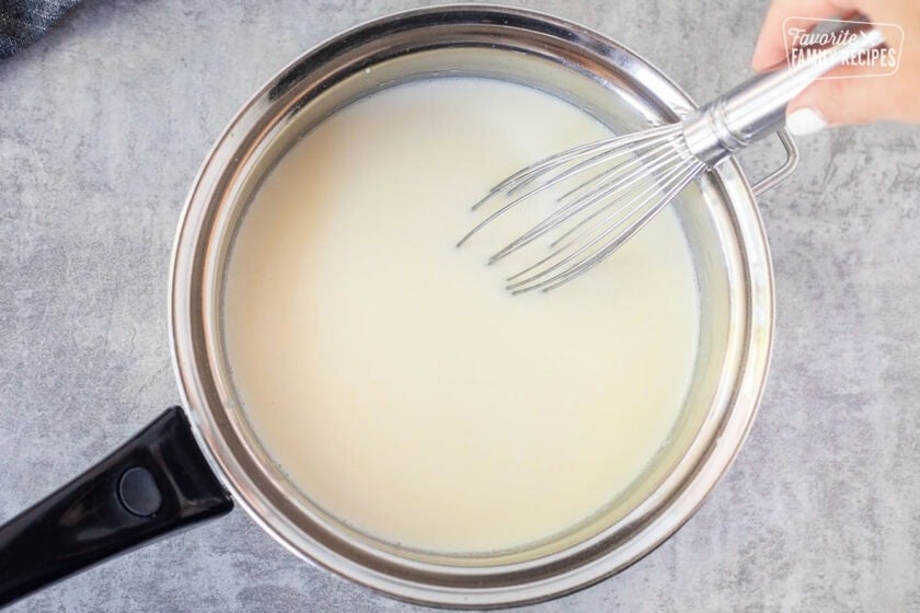 Whisking bechamel ingredients together in a saucepan.