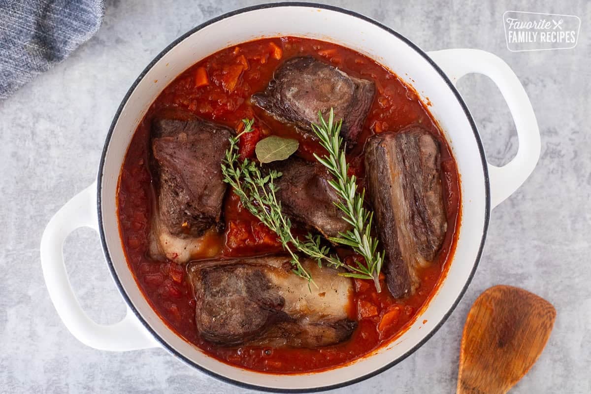 Dutch oven with meat and fresh herbs added to ragu sauce.