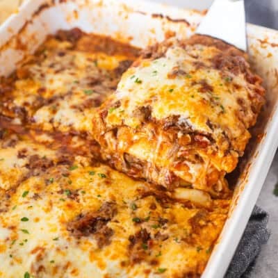 Lifting a cheesy slice of short rib lasagna from a baking dish.