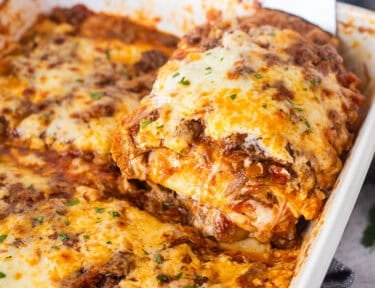 Lifting a cheesy slice of short rib lasagna from a baking dish.