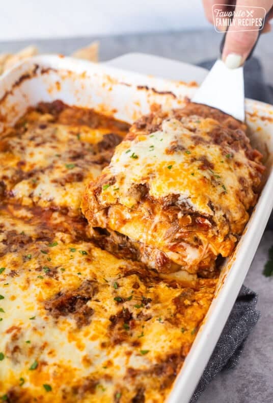 Lifting a cheesy slice of short rib lasagna from a baking dish.