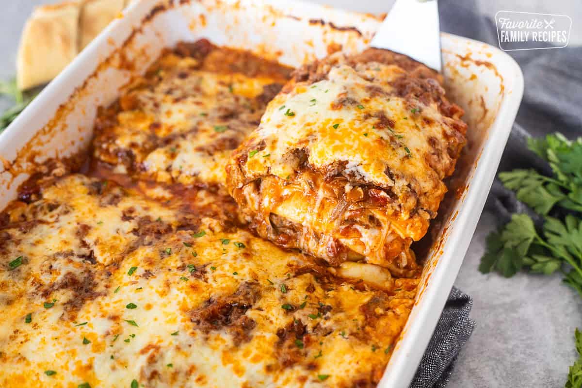 Lifting a cheesy slice of short rib lasagna from a baking dish.