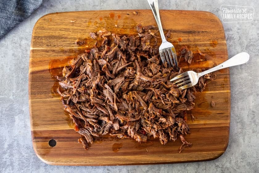 Shredded short rib meat on a cutting board with two forks.