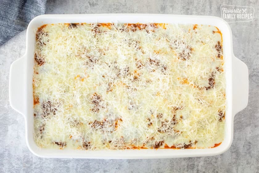 Top layer of short rib lasagna in a baking dish with béchamel and shredded cheese on top.