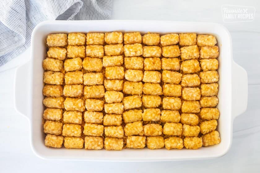 Placing frozen tater tots on top of ground beef mixture casserole and cheddar cheese.